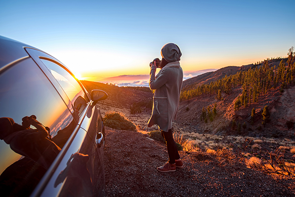 Woman photographing beautiful landscape above the clouds near the car on the sunset