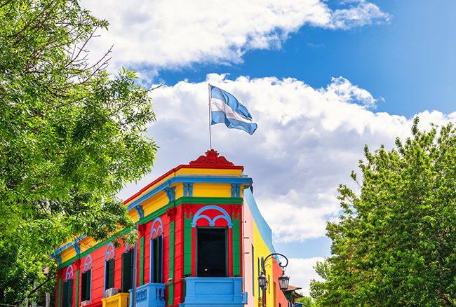 Typical brightly colored building on Caminito street in La Boca district, Buenos Aires, Argentina - Argentine flag on top of building with blue sky with clouds
